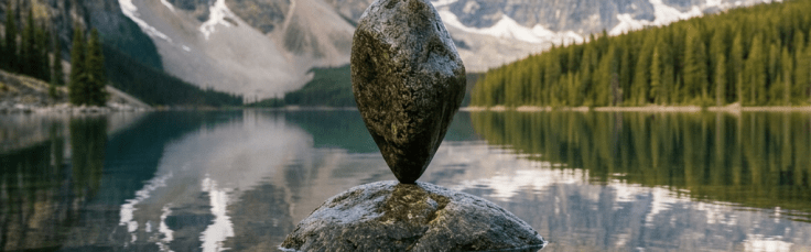 Rock balanced on another rock in calm lake with mountain and forest reflection